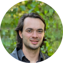 Portrait headshot of tutor John standing in front of green foliage.